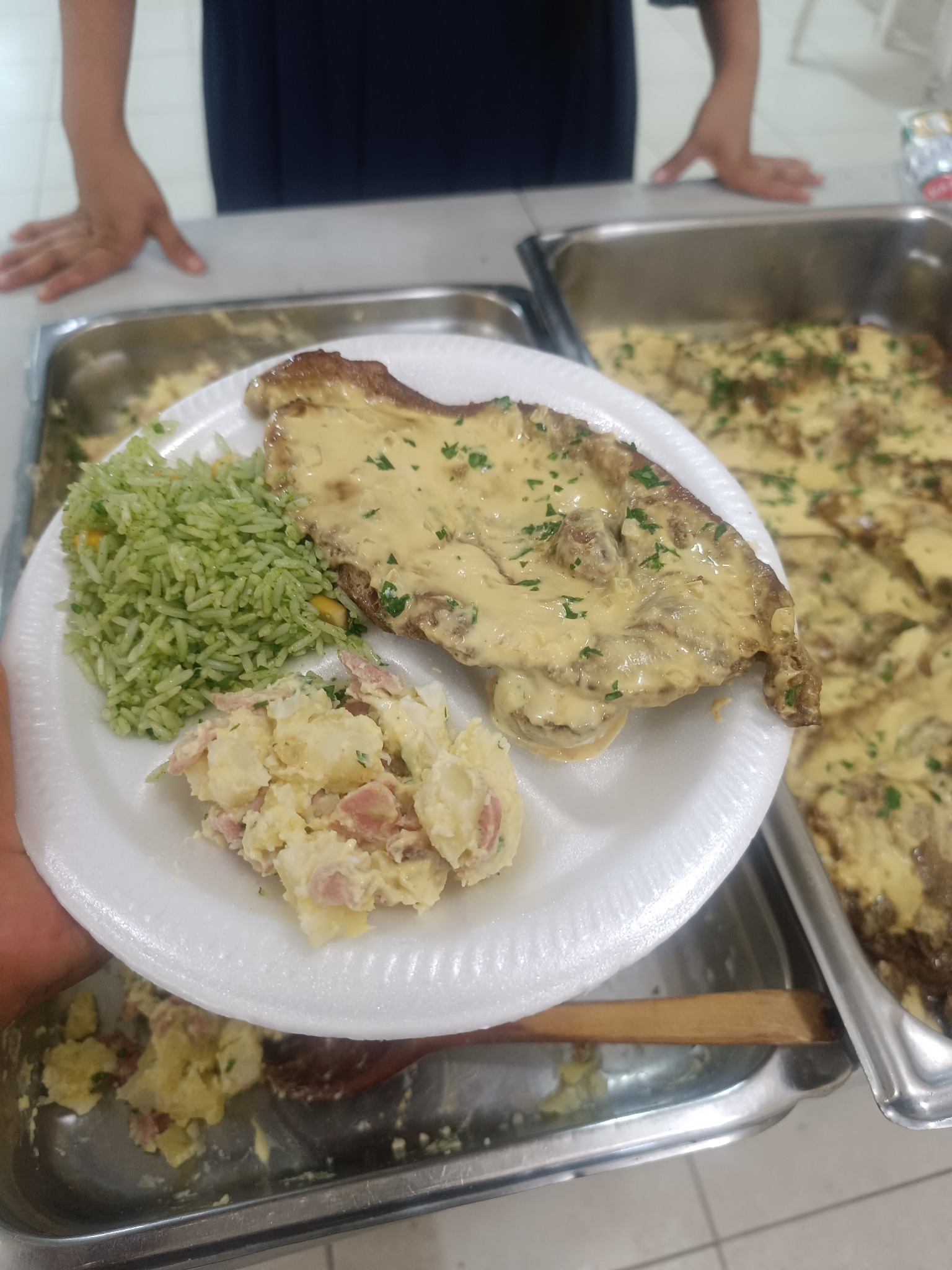 Plato de arroz verde con maíz, chuleta cubierta con salsa de mostaza y naranja, y ensalada de papa con Frankfurt.